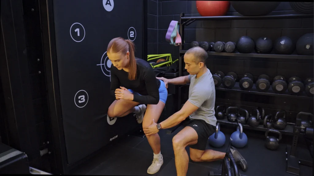 Personal trainer guiding a client through a supported lower-body movement assessment during a one-to-one training session