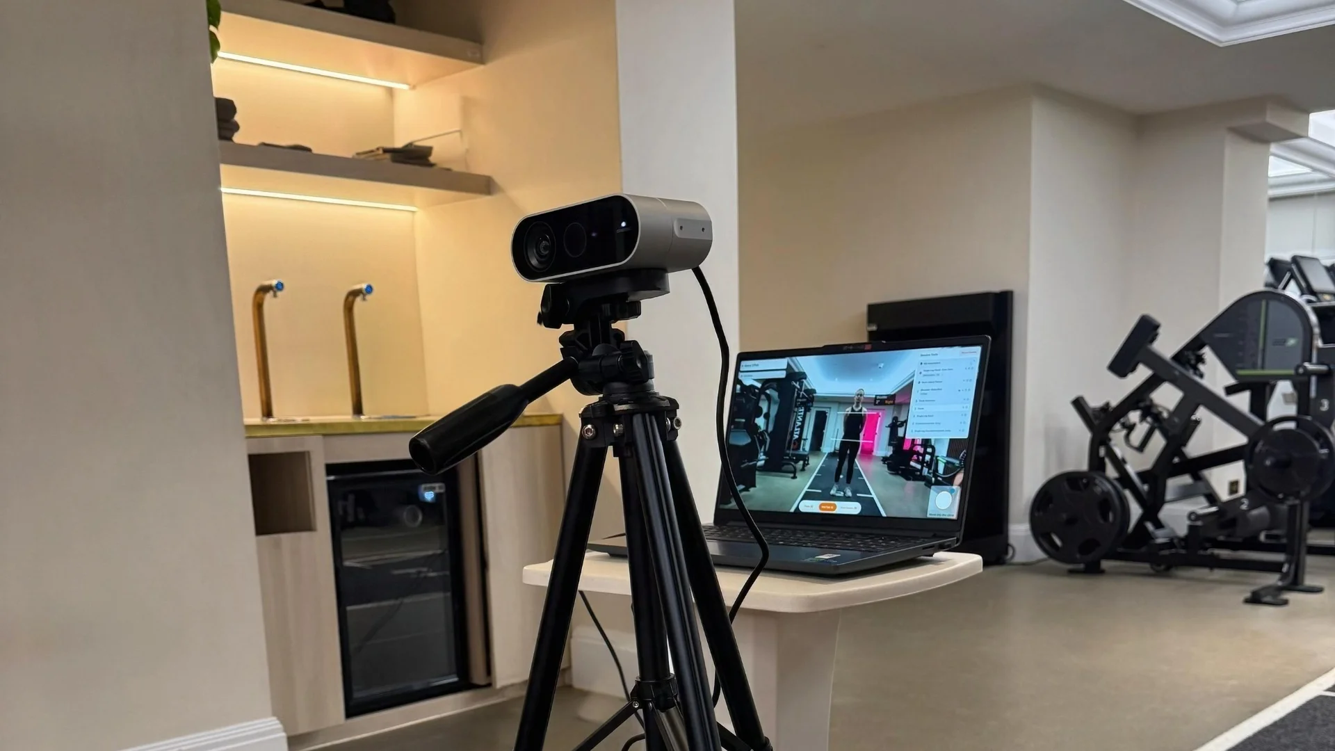 Camera set up on a tripod to record a client’s movement assessment, with analysis software displayed on a laptop in a gym environment
